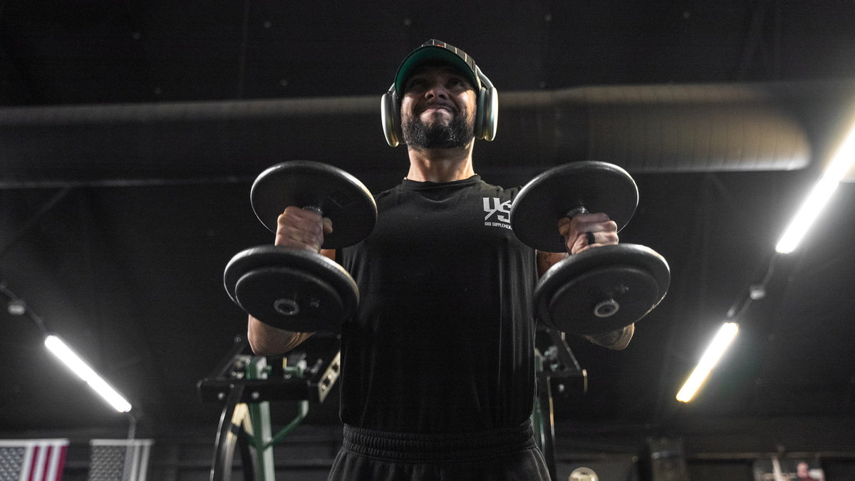 Lifter in headphones holding two dumbbells under gym lights