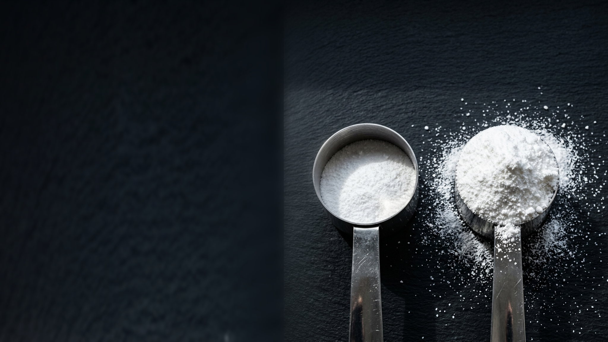 Two steel scoops of white powder on slate, the left only part full, the right heaped and spilling