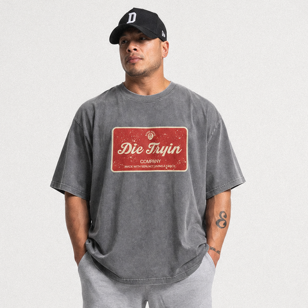Man in a black cap wearing a washed grey oversized tee with a red Die Tryin Company label graphic
