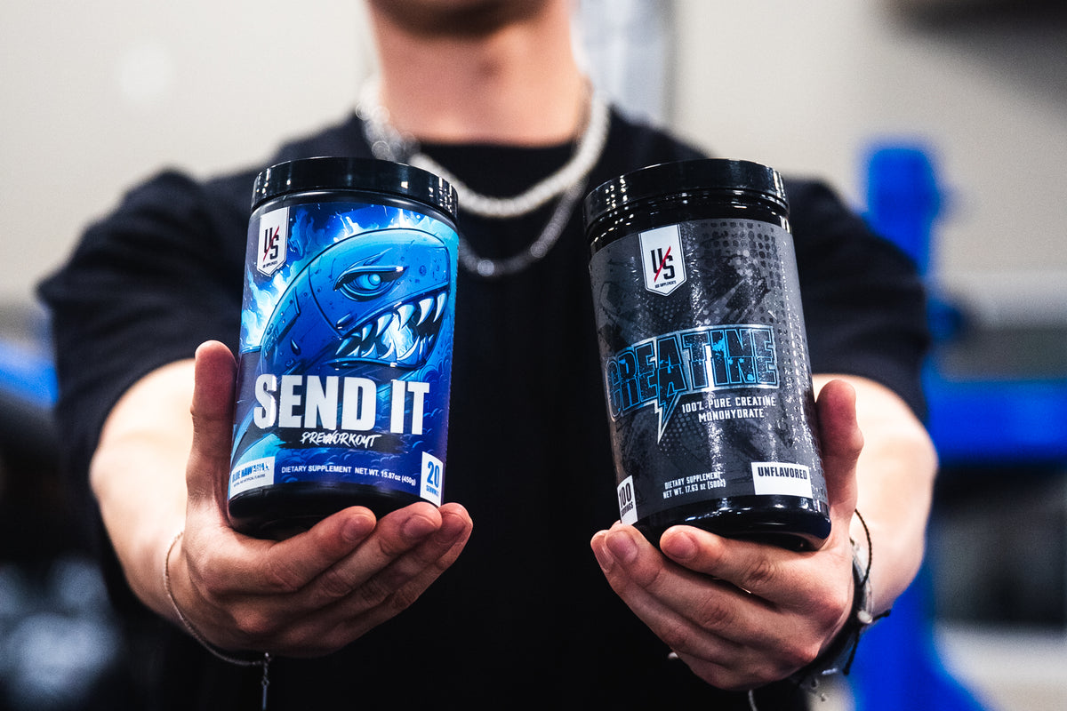 Person holding out a SEND IT pre-workout tub and an Unflavored Creatine tub toward the camera in a gym