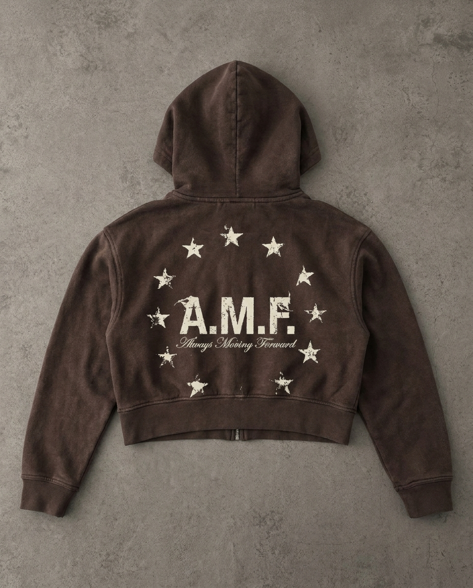 Flat lay of the back of a brown cropped zip-up hoodie, A.M.F. Always Moving Forward print in a ring of stars, on concrete