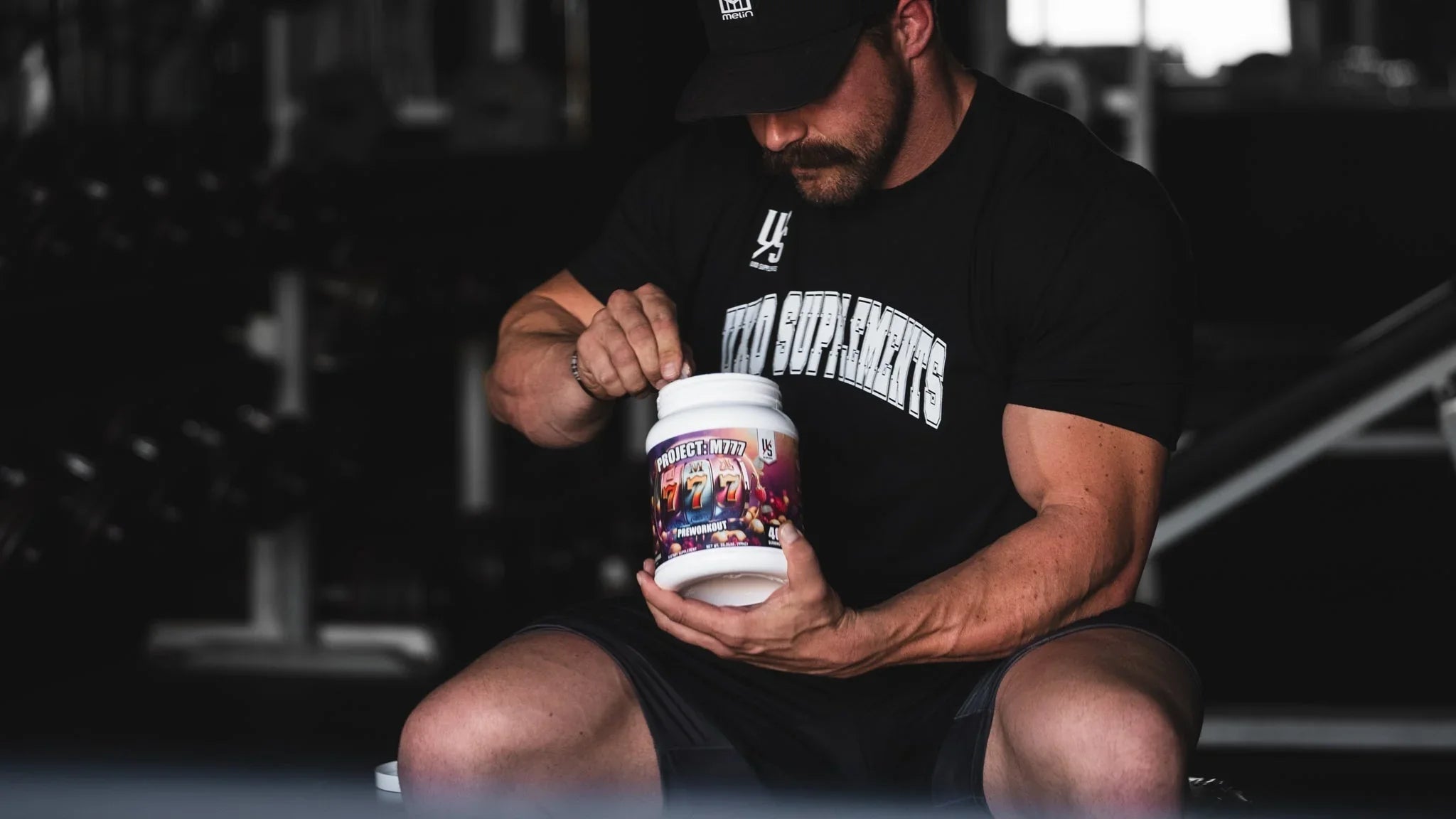 Lifter opening a tub of Project M777 pre-workout in the gym