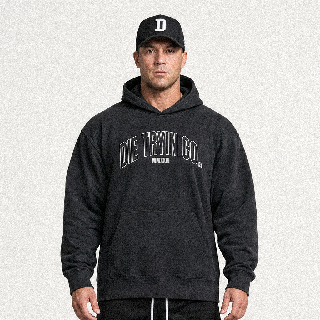 Man in a black cap wearing a black hoodie with an arched outlined Die Tryin Co. print, front view