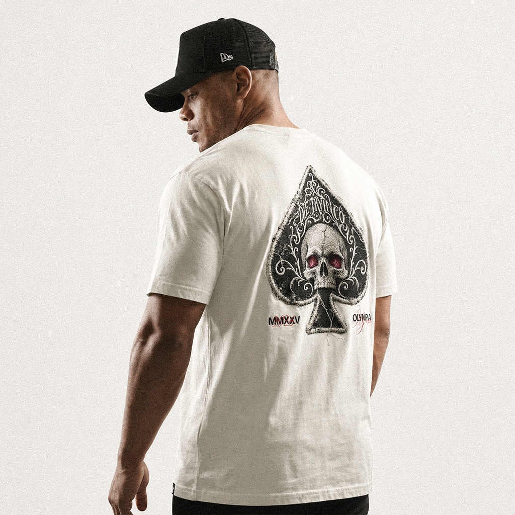 Back view of a man in a black cap wearing a white tee with a spade and red-eyed skull print