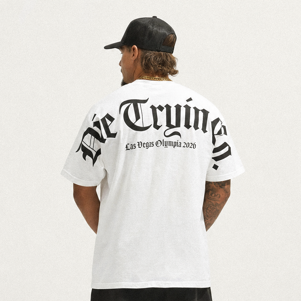 Back view of a man in a black cap and white oversized tee with a black gothic Die Tryin Co. Las Vegas Olympia 2026 print